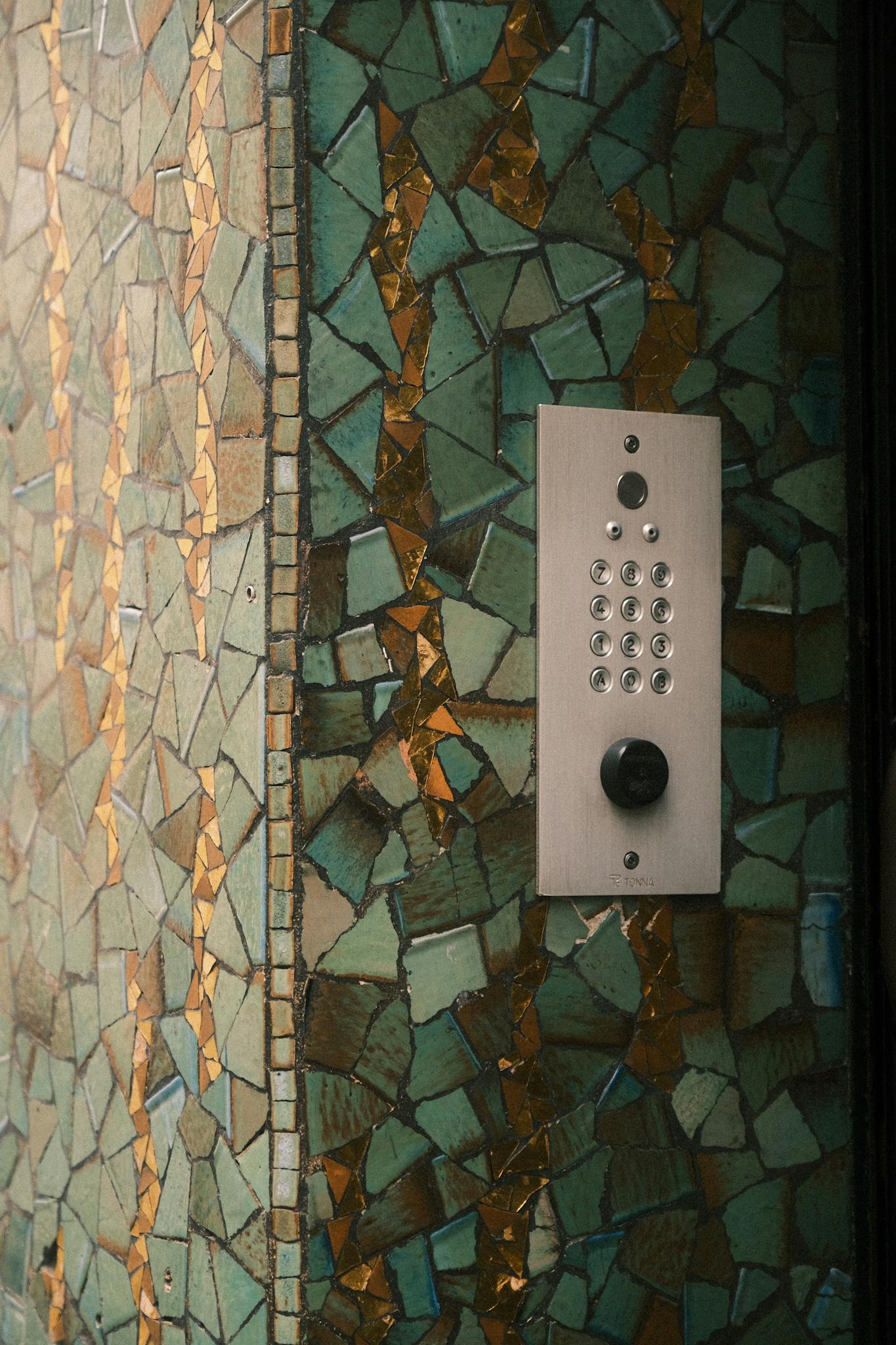 Close-up of a modern intercom on a decorative mosaic wall in an urban setting.